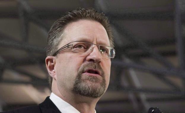 A bearded man speaks in a large auditorium.