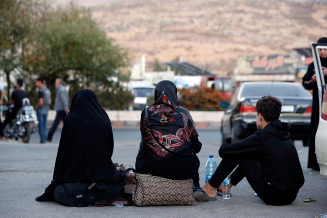 Lebanese people sit after crossing into Syria at the Syrian-Lebanese border crossing