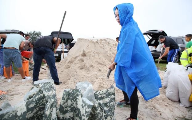 People in raincoats fill sandbags